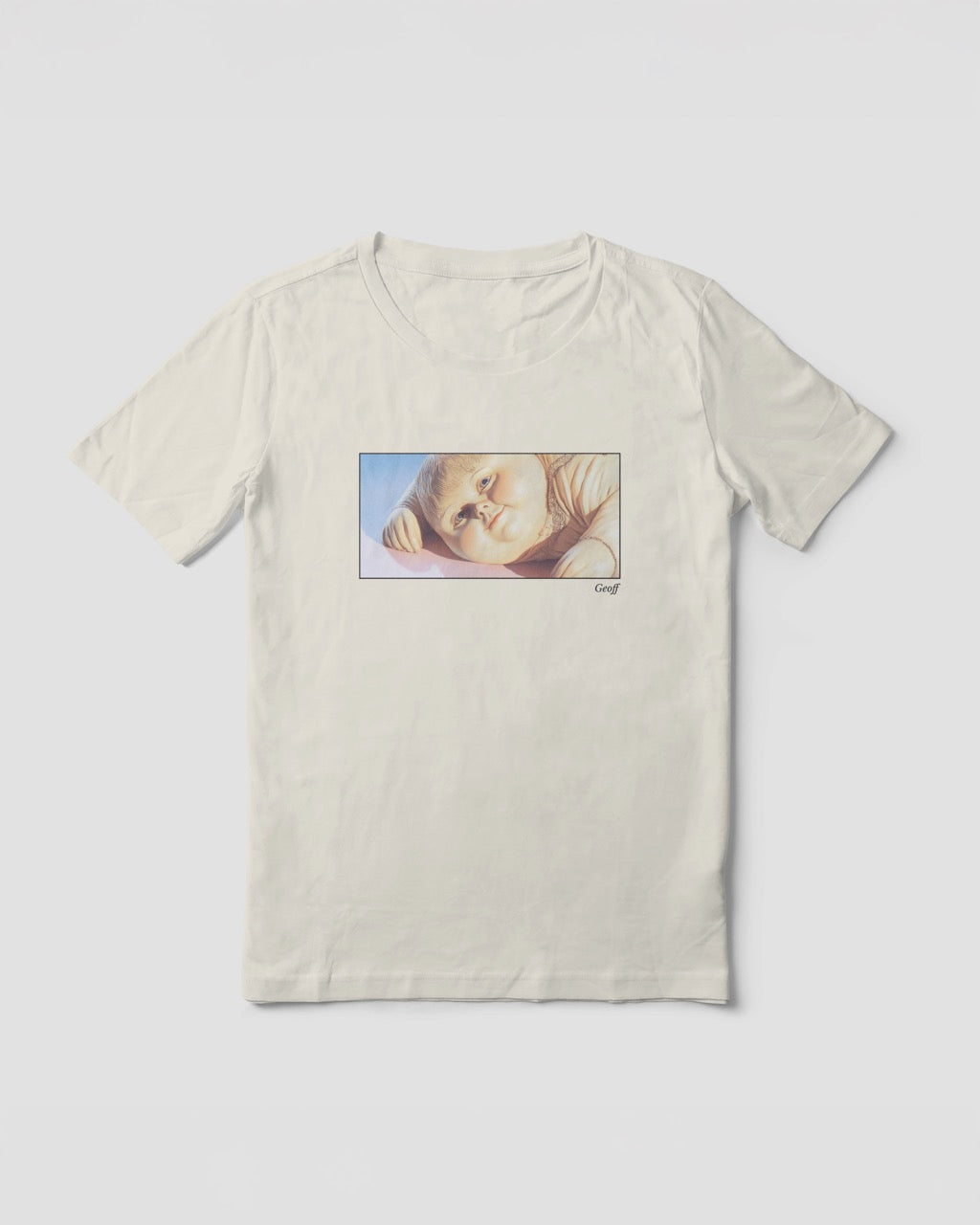 a light natural organic cotton t-shirt featuring a close-up, half-frame graphic print of a jolly, proud boy (Geoff) looking slightly upwards, with his name 'Geoff' subtly printed in Libre Baskerville below the image. The t-shirt has a dreamy aesthetic