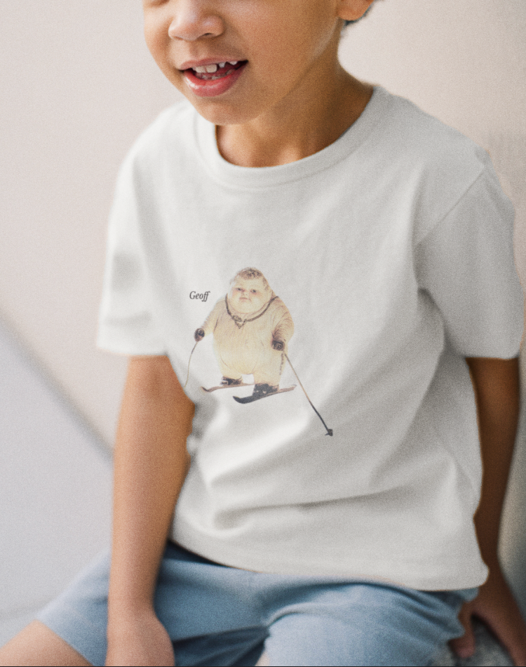Kid wearing white organic cotton Geoff & Jeffrey children’s t-shirt. The front of the shirt has a print of Geoff with skis