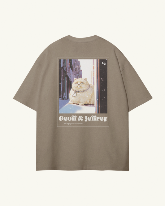beige organic cotton Geoff & Jeffrey unisex tee with drop shoulders  and a large graphic backprint of a joyful, fat cat in the city with snow, with the brandname in ohno blazeface and title in libre baskerville printed below.