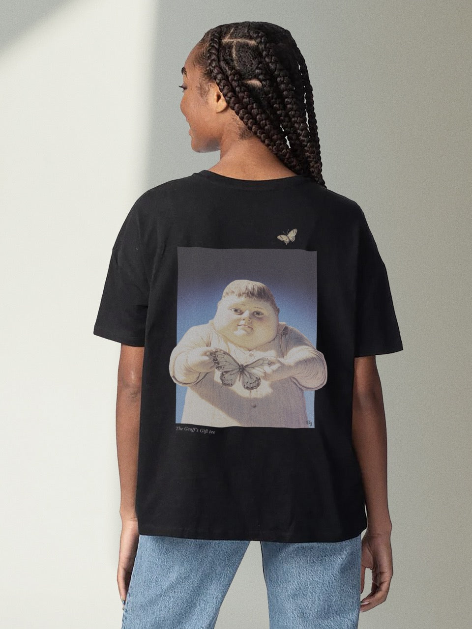 black organic cotton Geoff & Jeffrey unisex t-shirt with drop shoulders and a large graphic backprint of the jolly boy Geoff holding a butterfly,with the title printed below. The shirt has a cool aesthetic.