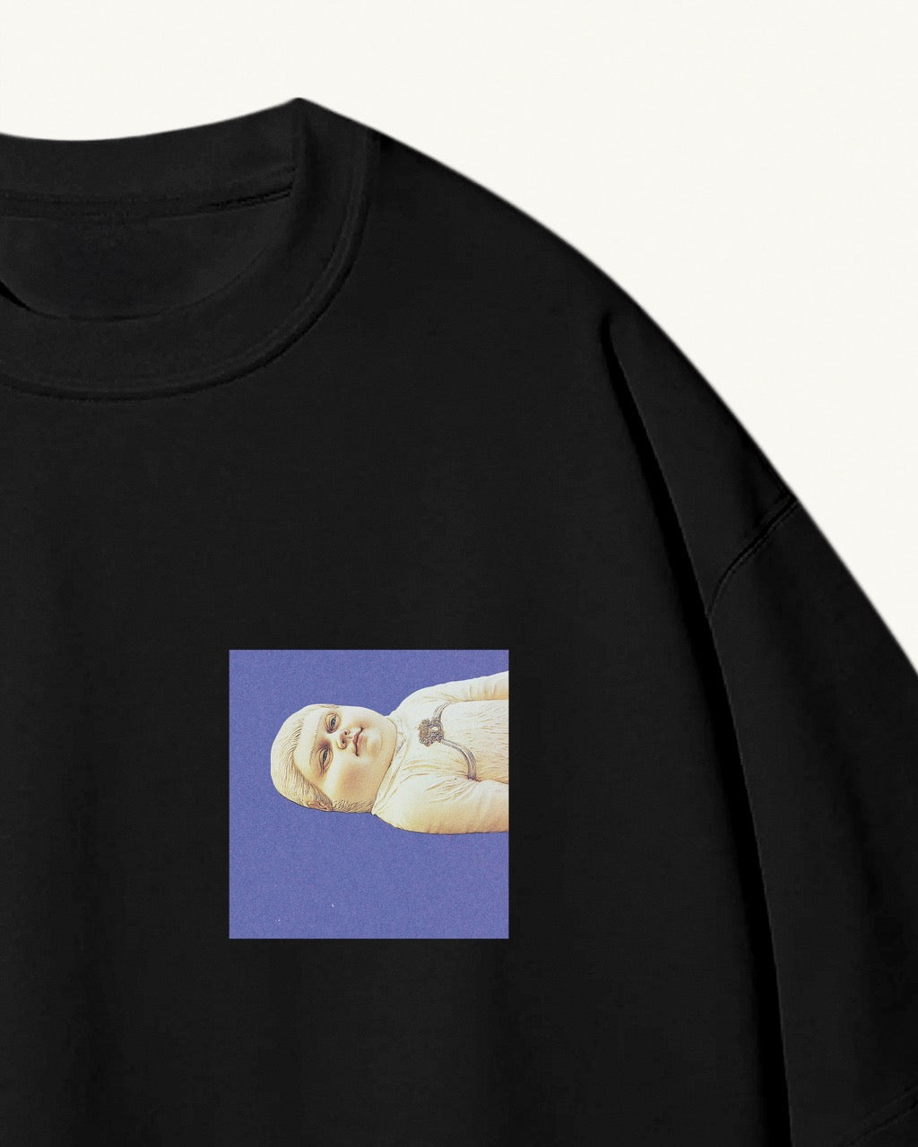 Close up of black organic cotton Geoff & Jeffrey, unisex t-shirt with drop shoulders and Geoff lying down on a blue square on the front. The shirt has a minimal design.