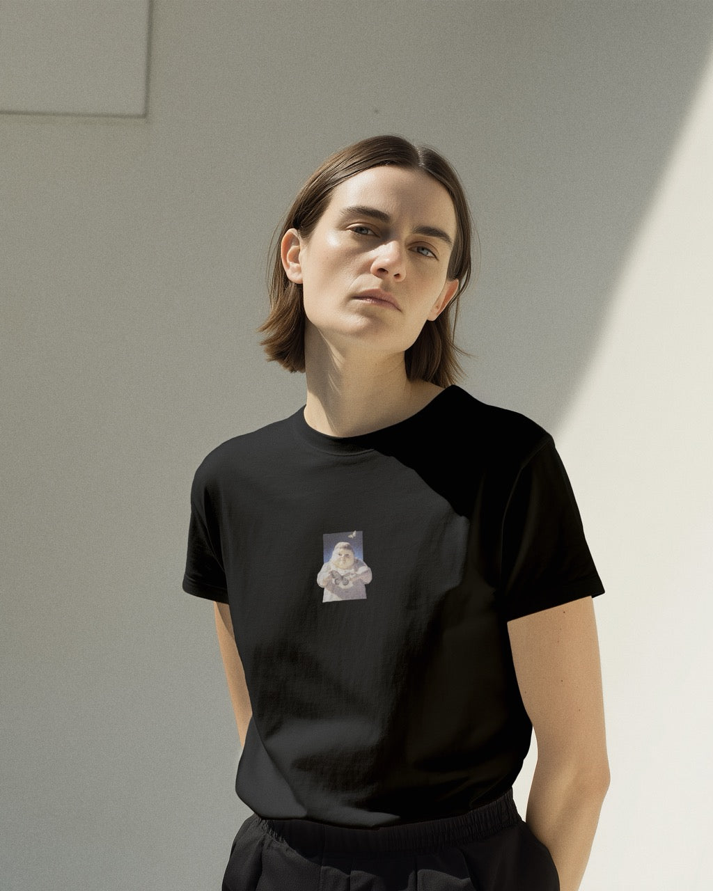 Model in women's black organic cotton Geoff & Jeffrey t-shirt with a small graphic print of a jolly, proud boy (Geoff) holding a butterfly in front of him. The t-shirt has a cute aesthetic.