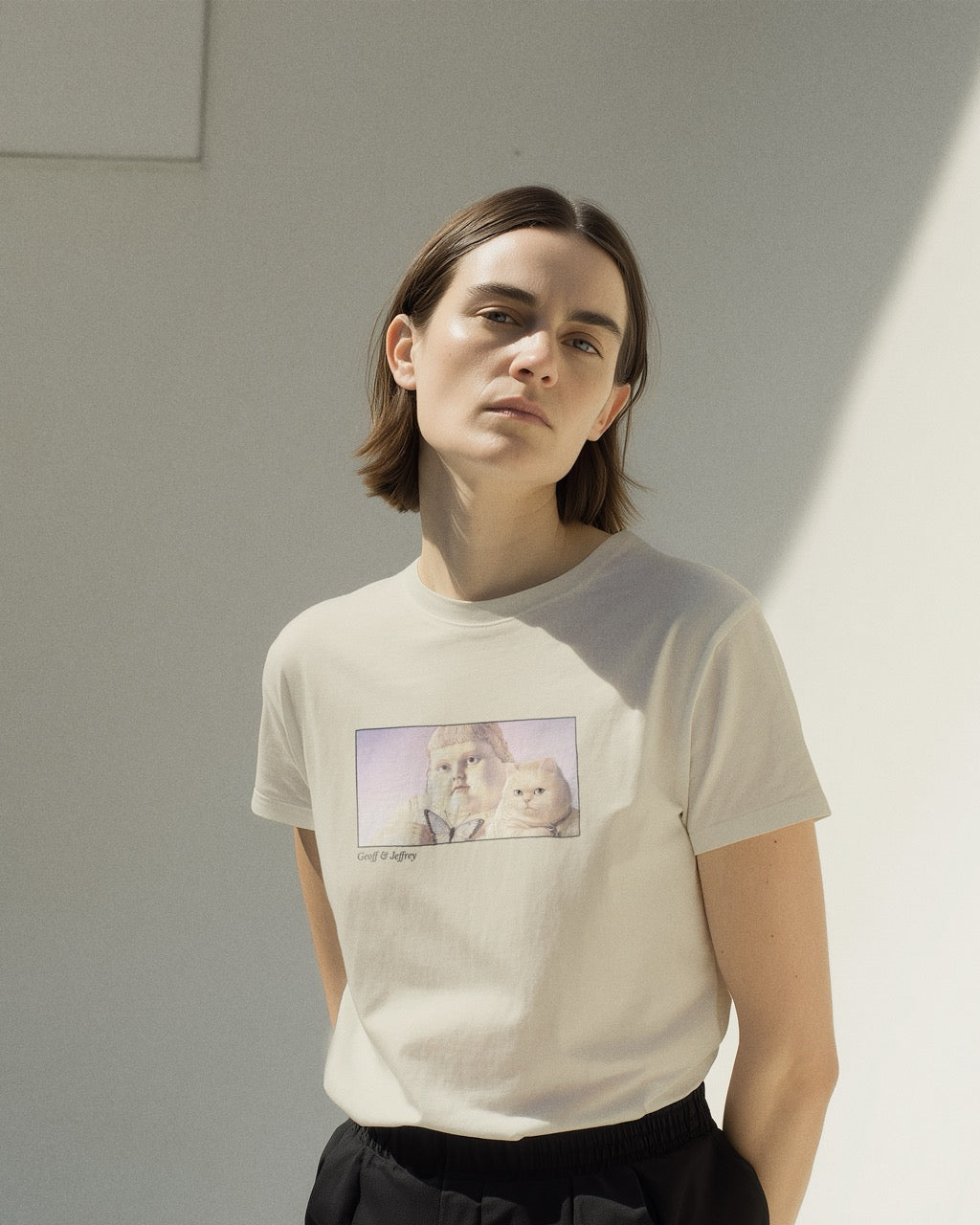 Women's off-white natural organic cotton Geoff & Jeffrey t-shirt with a framed graphic print of the jolly, proud boy (Geoff) and his funny fat cat (Jeffrey), holding a butterfly, with there names subtly printed in Libre Baskerville below the image. The t-shirt has a dreamy aesthetic.
