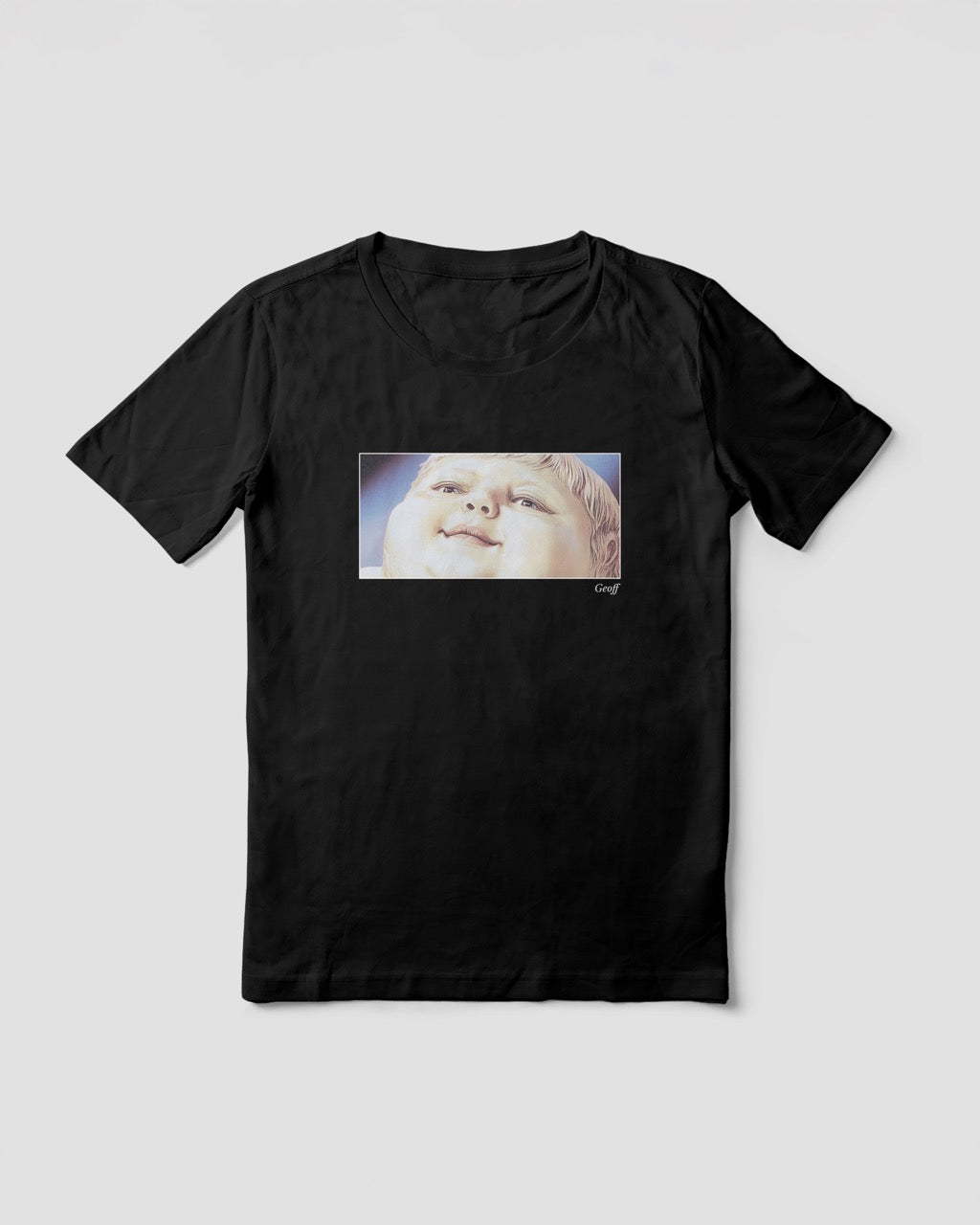 Women's black organic cotton Geoff & Jeffrey t-shirt with a framed graphic print of a jolly, proud boy (Geoff) looking upwards, smiling, with his name 'Geoff' subtly printed in Libre Baskerville below the image. The t-shirt has a feel good aesthetic