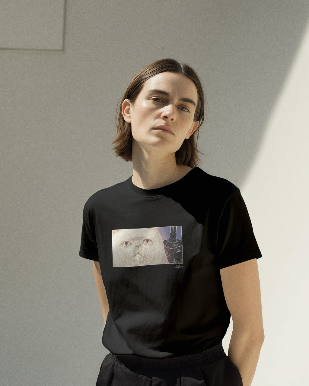 Model in women's black organic cotton Geoff & Jeffrey t-shirt with a framed graphic print of a funny fat cat (Jeffrey) poker-faced and a kettle at his side. With his name 'Jeffrey' subtly printed in Libre Baskerville below the image. The t-shirt has a cute aesthetic