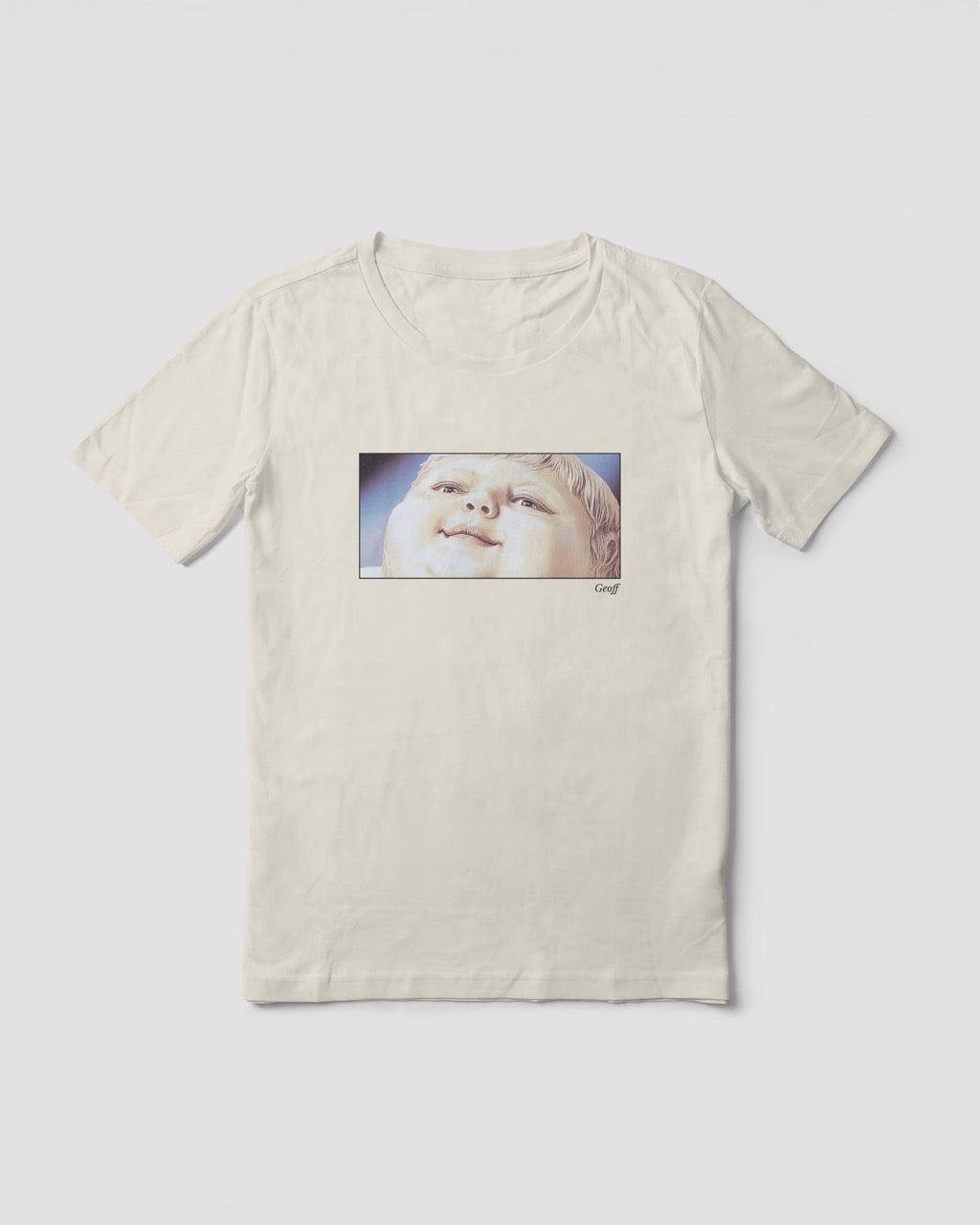 Women's off-white natural organic cotton Geoff & Jeffrey t-shirt with a framed graphic print of a jolly, proud boy (Geoff) looking upwards, smiling, with his name 'Geoff' subtly printed in Libre Baskerville below the image. The t-shirt has a feel good aesthetic