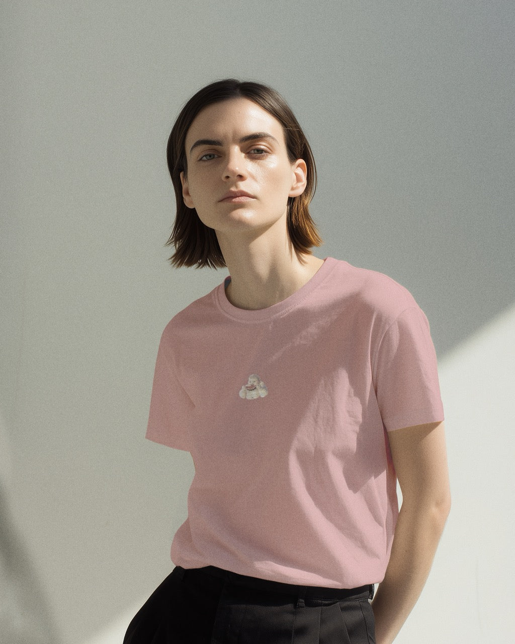 model in a women's soft pink organic cotton Geoff & Jeffrey t-shirt with a graphic print of a jolly, proud boy (Geoff) smiling and eating a watermelon, with his name 'Geoff' subtly printed in Libre Baskerville below the image. The t-shirt has a cute aesthetic.