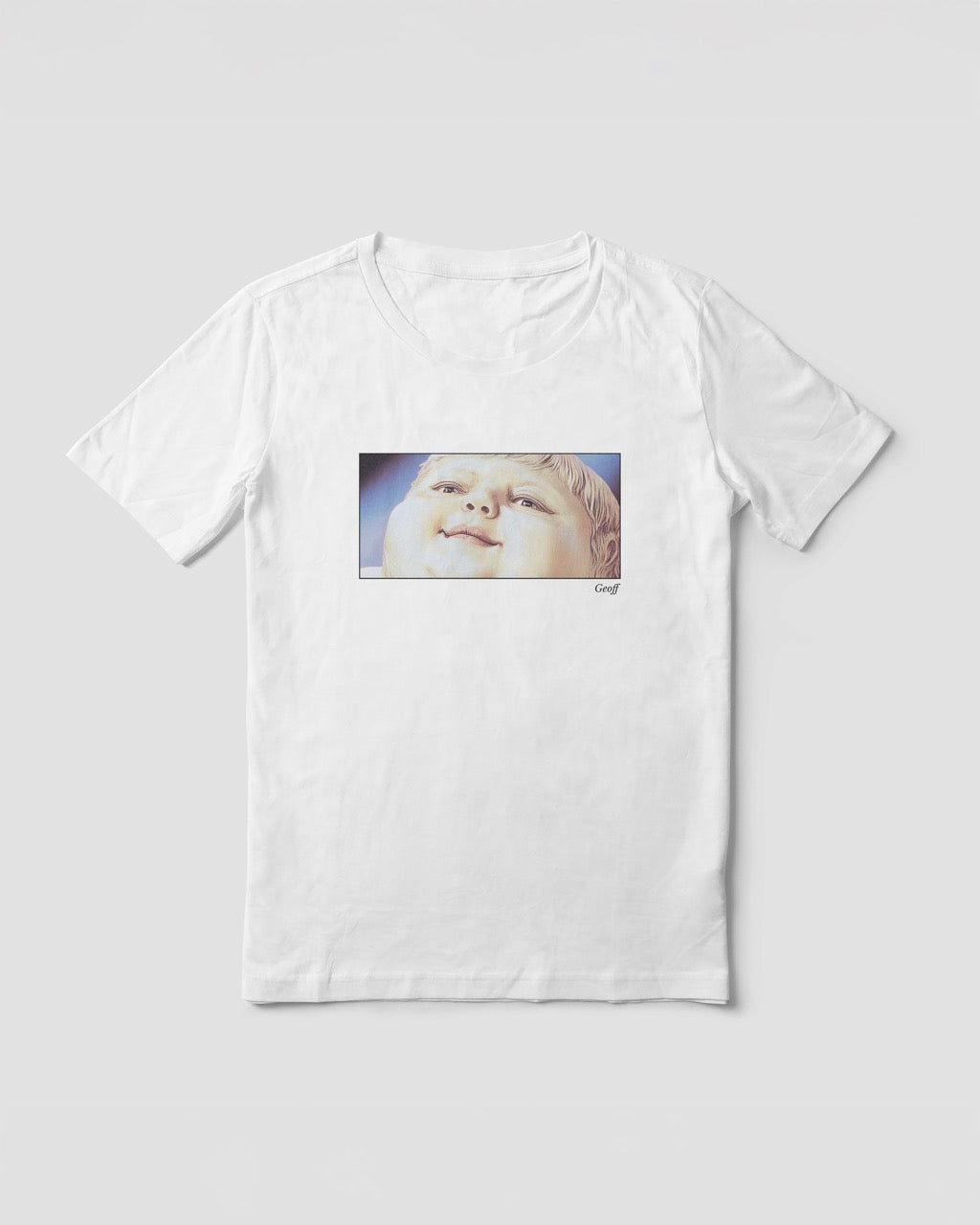 Women's white organic cotton Geoff & Jeffrey t-shirt with a framed graphic print of a jolly, proud boy (Geoff) looking upwards, smiling, with his name 'Geoff' subtly printed in Libre Baskerville below the image. The t-shirt has a feel good aesthetic